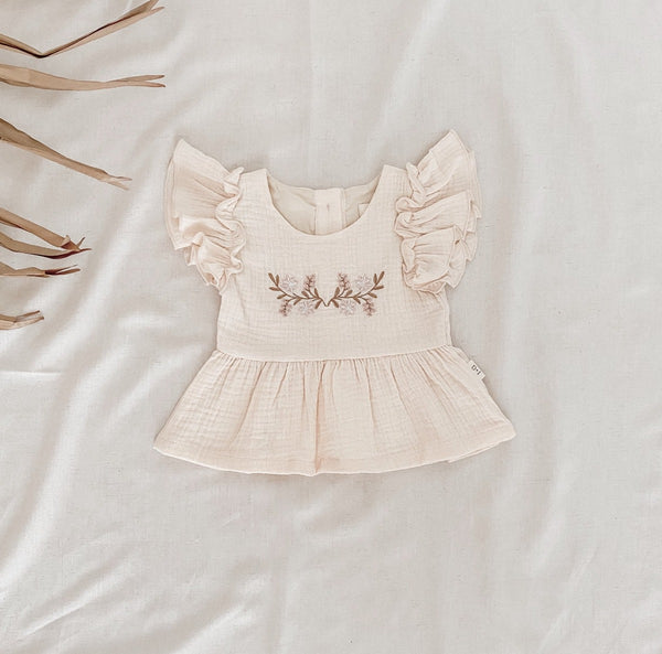 US stockist of India and Grace's Embroidered Ruffle Peplum Top in cream.  Made from cotton with shell buttons at the back, ruffle sleeves and floral embroidery on the chest. 