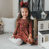 US stockist of Karibou Kids' Royal Visit Long Sleeve Pocket Dress in Cherry Red.  Made from cotton in a rich cherry red color with contrasting gold swirl print and ties at neck.