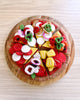 US stockist of Tara Treasures felt mushroom pizza slice. Felt pizza with vegetables on a wooden board against a checkered background.  