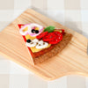 US stockist of Tara Treasures felt mushroom pizza slice. Felt pizza with vegetables on a wooden board against a checkered background.  