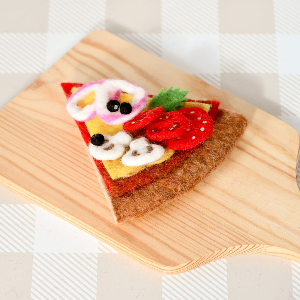US stockist of Tara Treasures felt mushroom pizza slice. Felt pizza with vegetables on a wooden board against a checkered background.  