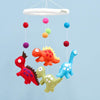 Colorful dinosaur mobile with hanging pom-poms against a light blue background.  US stockist of Tara Treasures.