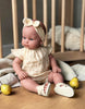 US stockist of Minikane's Yaelle Bambini doll dressed in her Helene Clara romper, matching headband and cream sandals.