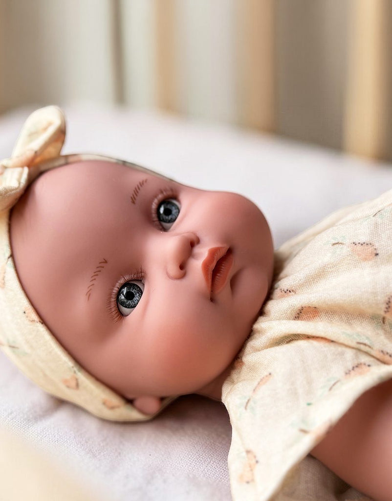 US stockist of Minikane's Yaelle Bambini doll dressed in her Helene Clara romper, matching headband and cream sandals.