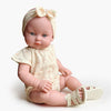 US stockist of Minikane's Yaelle Bambini doll dressed in her Helene Clara romper, matching headband and cream sandals.