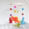 Colorful dinosaur mobile with hanging pom-poms against a light blue background.  US stockist of Tara Treasures.