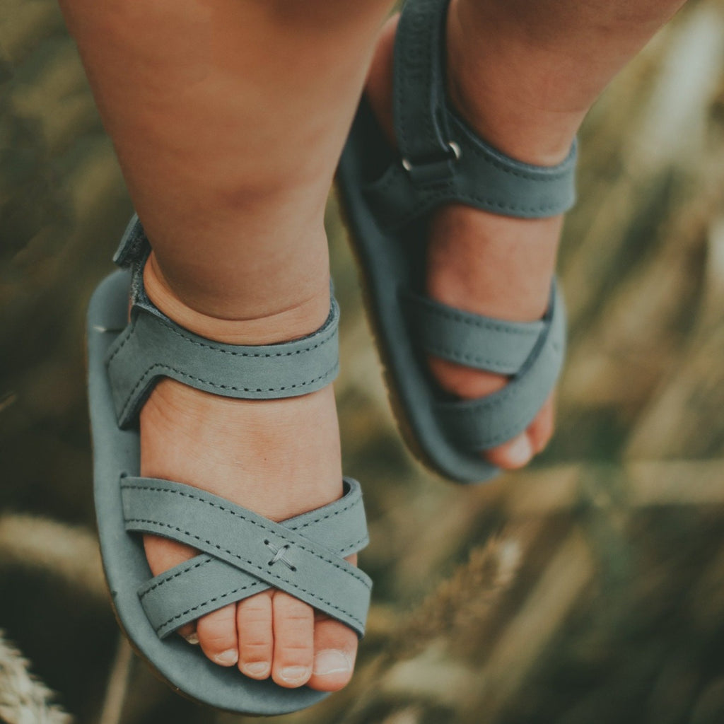 US stockist of Donsje USA's Giggles premium handmade leather nubuck sandals.  Petrol Grey in color with velcro fastening at back.  Sizes 0-12 mths have soft sole, 12-30mths have a soft flexible, rubber sole.
