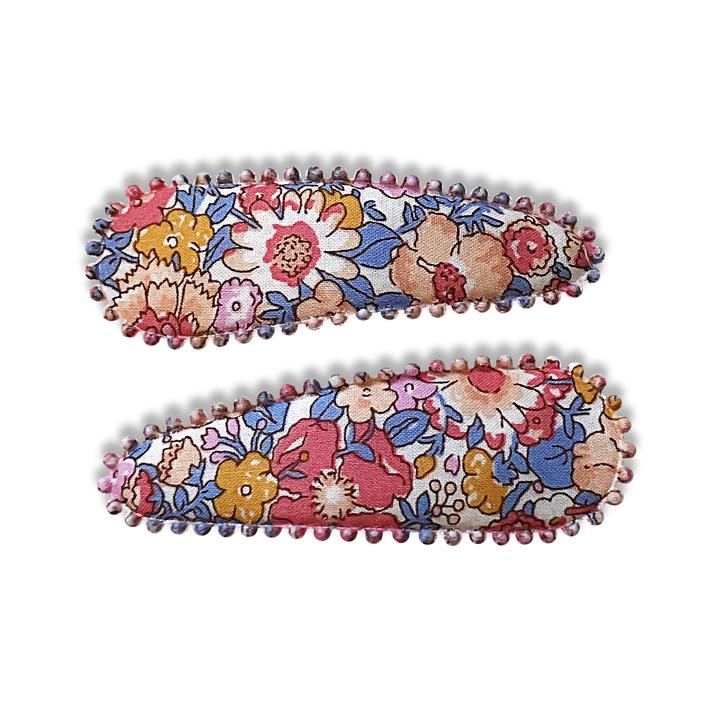 US stockist of Josie Joan's Amelia fabric hair clips.  Set of two fabric hair clips made from pale coloured fabric with multicolored flowers and  contrasting blue leaves.  Has scalloped edging.