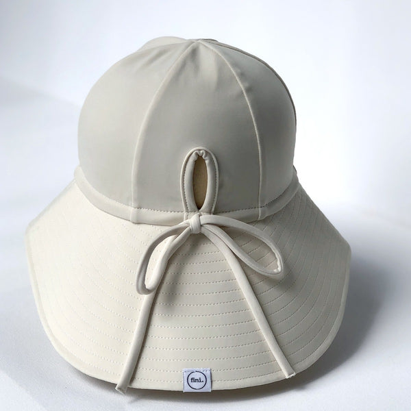 US stockist of Fini the Label's gender neutral, floppy swim hat in cream. Features elongated back for added sun protection, chin strap and adjustable bow around crown for better fit. Brim is medium stiffness and can be flipped up at front.  Made from nylon/spandex and is quick drying.