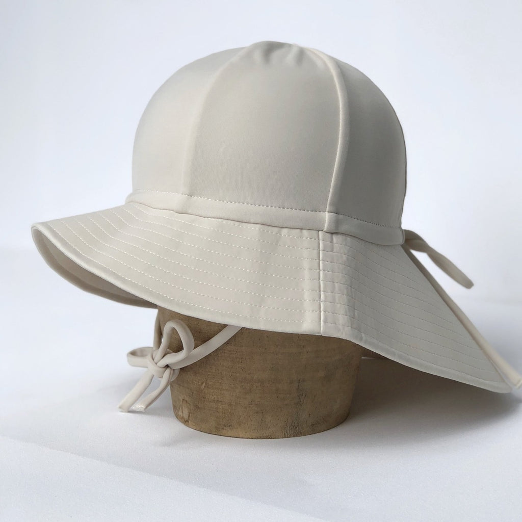US stockist of Fini the Label's gender neutral, floppy swim hat in cream. Features elongated back for added sun protection, chin strap and adjustable bow around crown for better fit. Brim is medium stiffness and can be flipped up at front.  Made from nylon/spandex and is quick drying.