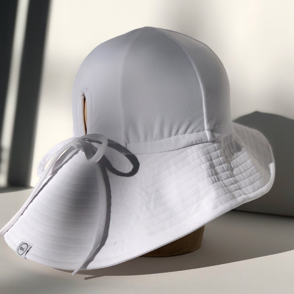US stockist of Fini the Label's gender neutral floppy swim hat in white. Features elongated back for added sun protection, chin strap and adjustable bow around crown for better fit. Brim is medium stiffness and can be flipped up at front.  Made from nylon/spandex and is quick drying.