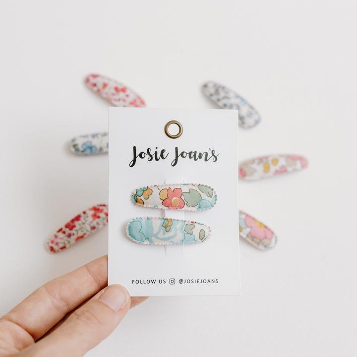 US stockist of Josie Joan's Little Kylie set of two fabric baby hair clips.  Cream colored fabric with blue, green flowers and red, yellow berries. Features scalloped edges.