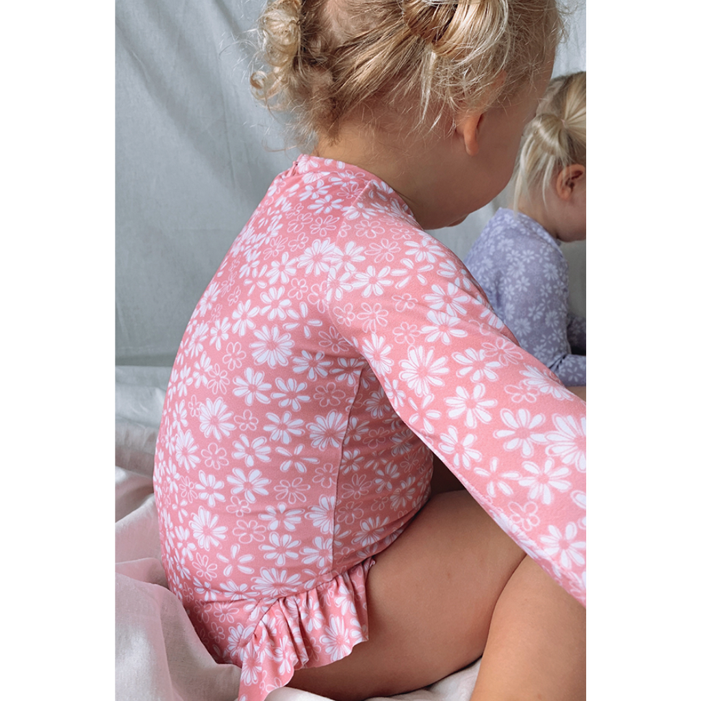 US stockist of Salty Swimwear's Zoe long sleeve rashsuit in pink daisy days.  Made from pink UPF 50+ recycled Repreve fabric with pretty white daisy print. Fully lined, with invisible back zipper and signature Salty frill on legs.