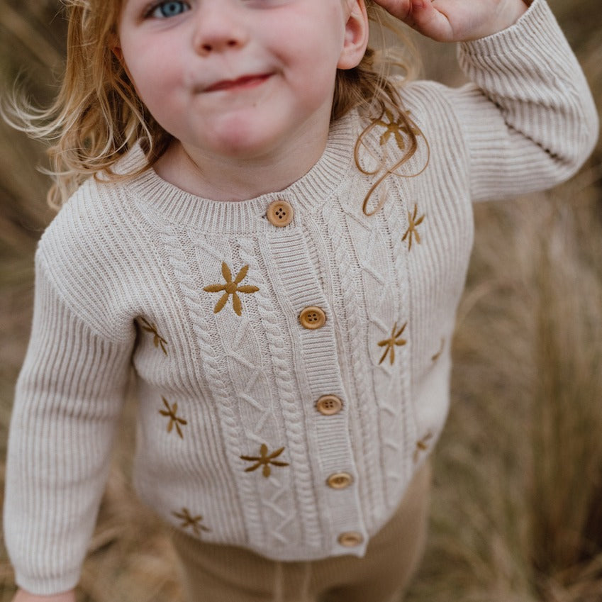 US stockist of Grown Clothing's Flower Field Cable Cardigan.  Made from 100% organic cotton with wooden buttons down front.  Oatmeal color with machine embroidered gold flowers.