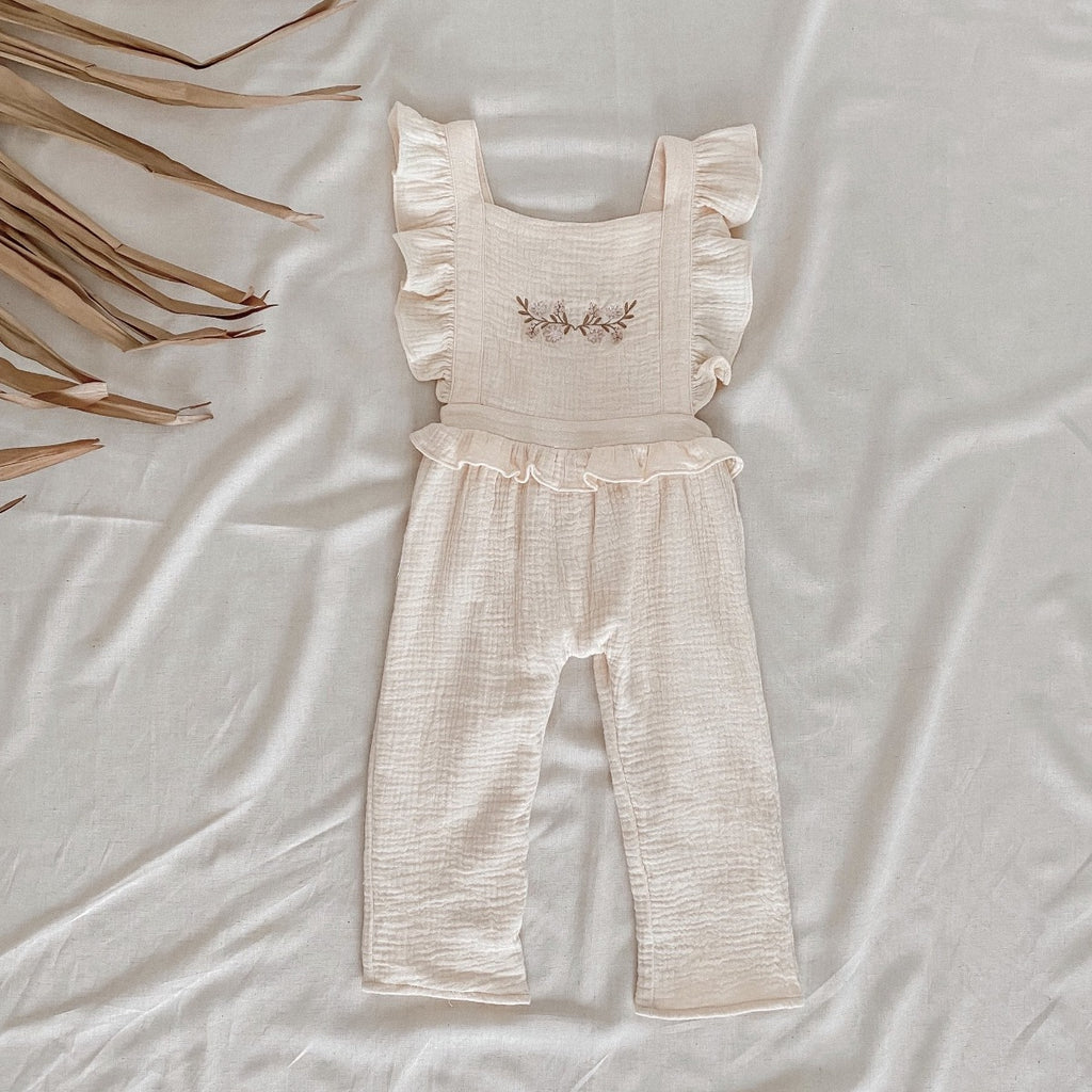 US stockist of India and Grace the Label's cream embroidered ruffle jumpsuit.  Features ruffle straps that cross over the back, floral embroidery on the chest, ruffle at waist and 3/4 legs.  Made from double cotton gauze.