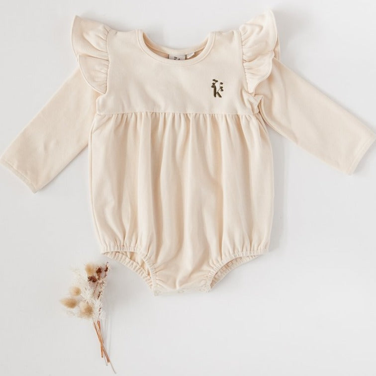 US stockist of Karibou Kid's Milana Winged Playsuit in almond cream.  Made from soft cotton, featuring long sleeves and ruffled wings at shoulders.