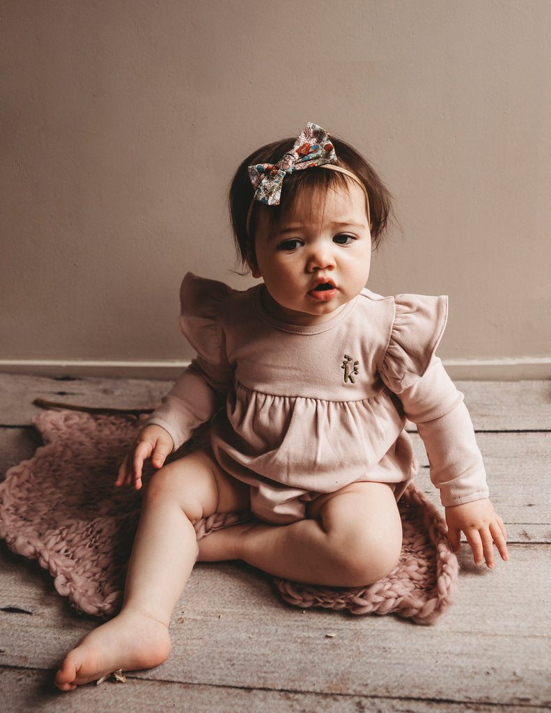 US stockist of Karibou Kid's Milana Winged Playsuit in soft pink.  Made from soft cotton, featuring long sleeves and ruffled wings at shoulders.