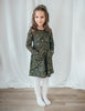 US stockist of Karibou Kids' Royal Visit Long Sleeve Pocket Dress in Emerald.  Made from cotton in a rich emerald green color with contrasting gold swirl print and ties at neck.